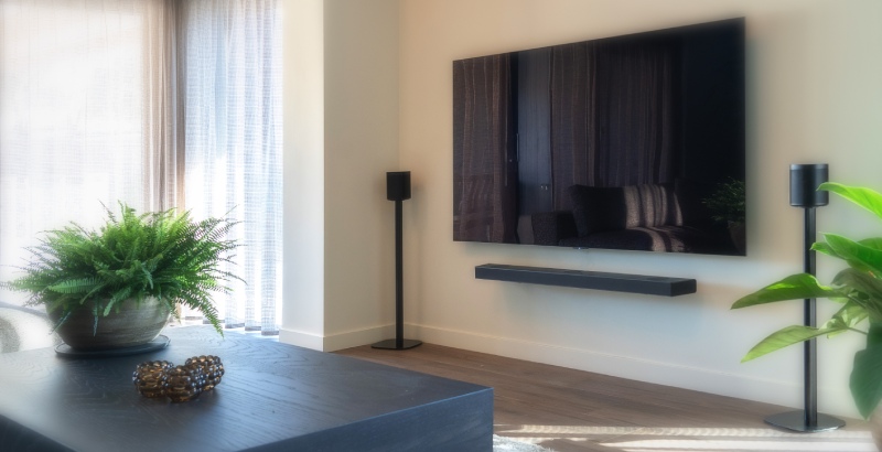 ¿Cómo se deben colocar los altavoces? Lea todo al respecto. Un televisor en la pared con dos altavoces a cada lado sobre soportes en el salón.