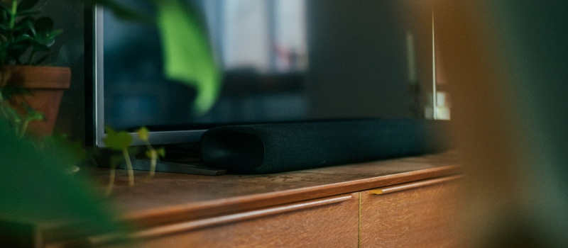 Lleva tus noches de cine a un nuevo nivel con una barra de sonido Primer plano de una elegante barra de sonido oscura sobre un mueble de madera.